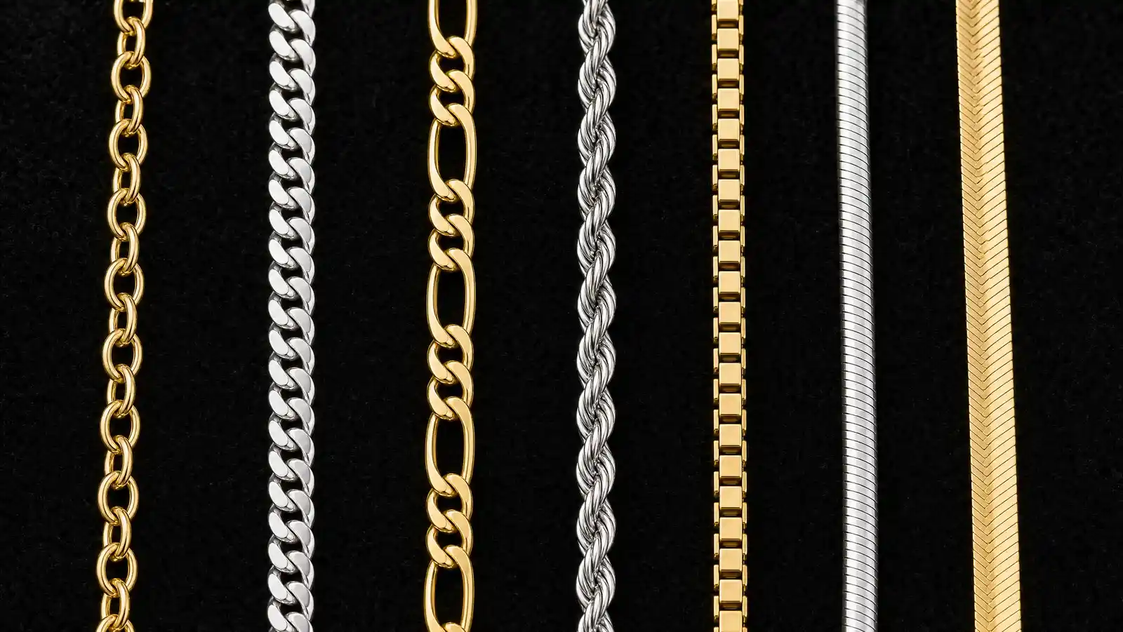 Seven necklace chain link styles laid side by side on black velvet including cable curb figaro rope box snake and herringbone